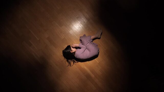 Young sad girl curled up on wooden floor under dim light symbolizing loneliness, depression, emotional pain and childhood trauma in a dramatic and moody composition