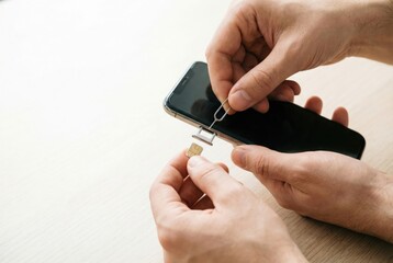 Fototapeta premium A person uses a special tool to open the tray and insert a nano SIM card into a modern smartphone.