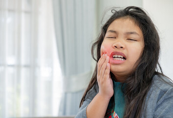Fototapeta premium Asian little girl suffering from toothache and dental pain touching her cheek, unhappy child having sensitive teeth or cavity problem, healthcare and dentistry concept.