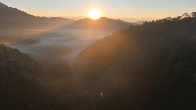 A captivating 1080p horizontal drone footage capturing a dynamic forward flight over a magnificent mountain range. The drone moves majestically towards the rising sun, which bathes the rugged peaks an