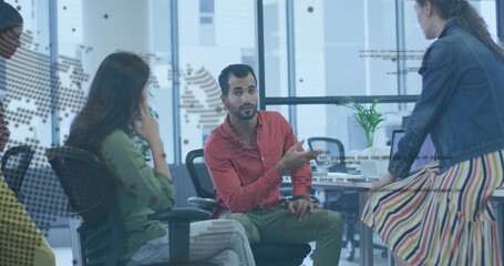 Obraz premium Gesturing man in red shirt speaking with colleagues at office meeting table, with dotted world map