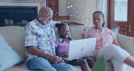 Smiling child wearing light purple T-shirt using silver laptop at home, seniors in plaid and pink