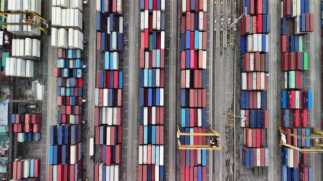 Top-down drone view over Manila Port showing stacked shipping containers, service lanes, and gantry cranes moving along terminal rows.