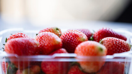 Strawberries in a plastic container on a wooden table. Selective focus.