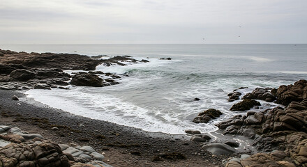 Ocean waves crash against rocky shore on overcast day, creating foamy surf and peaceful atmosphere near the coast, evoking a sense of tranquility.