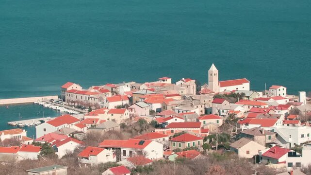 Steady elevated wide-angle footage showing most of the central coastal town with red rooftops, church tower and the blue Adriatic Sea on a bright sunny day in the Zadar region of Croatia.