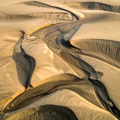 Winding stream cuts through sandy dunes, creating striking texture and shadow play