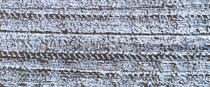 Aerial texture of tire tracks and machinery marks in a snowy field creating a linear industrial pattern in winter