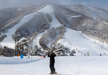 Snowboarder standing on a groomed run overlooking the slopes of Madarao, Japan