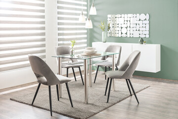 Fototapeta premium A tastefully appointed modern dining room with a glass table and chairs, situated in front of a large window with the grey blinds pulled up