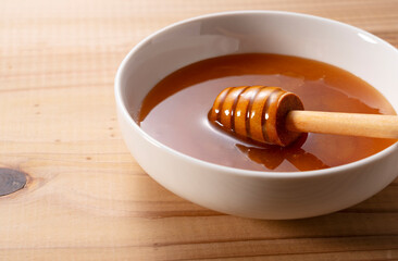 Wooden honey dipper resting in a white ceramic bowl filled with thick Manuka honey on a wooden table.