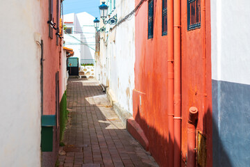 Naklejka premium Narrow alleyway features vibrant stucco walls with traditional ironwork and brick paving. Picturesque scene captures typical old-world Mediterranean architecture found in historic European towns