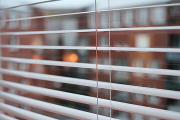 A window with white blinds is shown with a city in the background