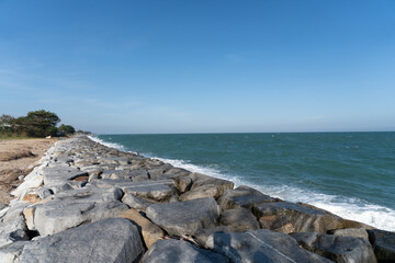 Peaceful landscape view with strong rock barrier protecting coast against blue sea wave under clear sky on bright sunny summer day