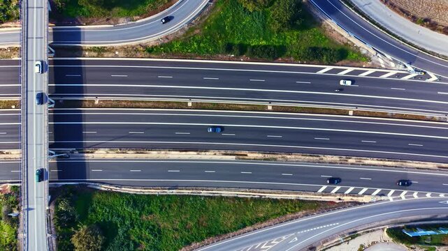 Vehicles navigate a complex highway interchange under clear skies. Roads branch out and lead to various destinations in a city during the day.