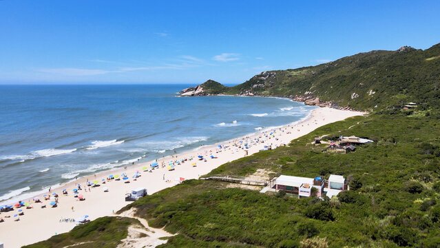 Panoramic aerial view of Mole Beach in Florianopolis, Santa Catarina, during the peak summer season, with a crowded beach and turquoise sea.
