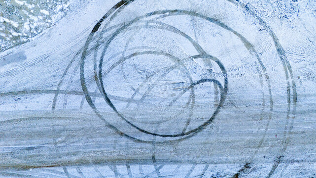 Top down aerial texture of a snowy ground with circular tire tracks creating an abstract geometric pattern in a winter industrial yard