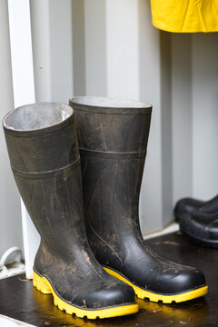 Black waterproof rubber boots stand on a dark floor in a storage shed. Ideal for wet weather safety, outdoor work gear, and industrial apparel themes.