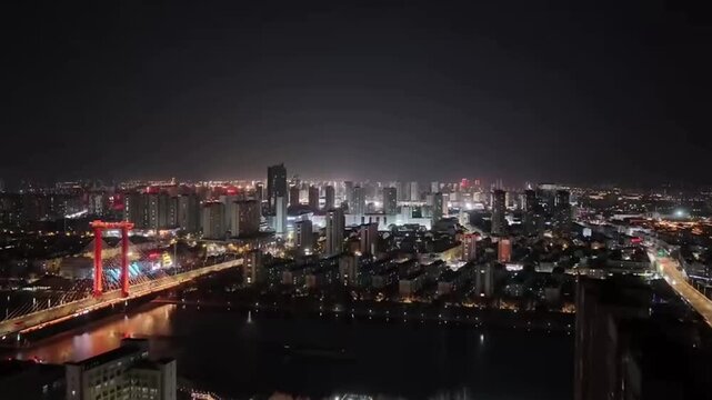 A stunning cinematic 1080p drone footage flying forward over a modern Chinese city at night. The shot captures a spectacular skyline of illuminated skyscrapers reflecting on a wide river. Below, a maj
