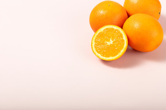Close-up of fresh, vibrant oranges, one cut in half, casting soft shadows on a pale pink background with copy space