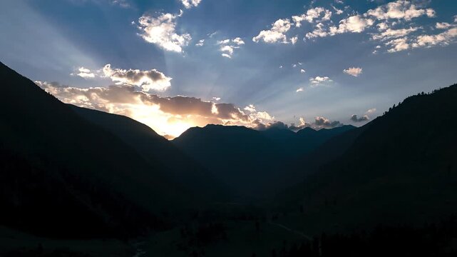 Silhouette Mountain Sunset, Cinematic drone timelapse moving over river valley during golden hour with godrays making dramatic pattern in the sky