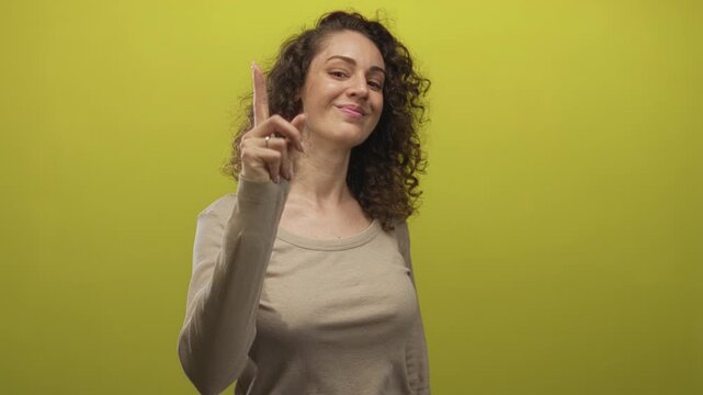 Woman pointing index finger at camera with hand to face and slight smirk in lime green studio; confidence.
