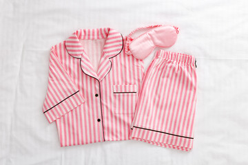 Striped Pink White Pajama Set with satin pink sleep mask on white sheet. Top view stylish woman home sleepwear from soft cotton on bedclothes. Cozy pyjamas of shirt, shorts for sleeping, flat lay