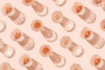 Minimal summer party concept, glasses of rose wine or champagne on pink with shadows and light reflections. Bright shine wineglass with sparkling alcohol drink at sunlight, top view monochrome pattern