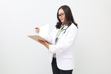 Fototapeta premium Asian adult female doctor standing wearing doctor's coat, stethoscope around neck, reading patient's medical record while smiling, standing isolated on white background.