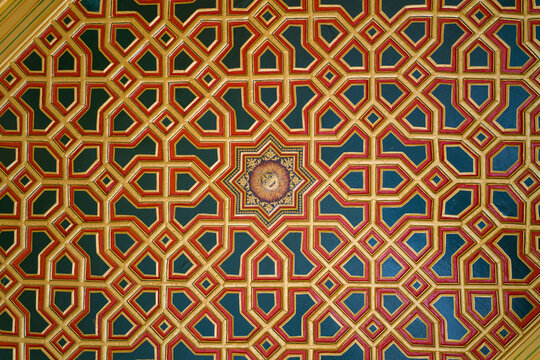 Elaborate ceiling design at Junagarh Fort in Bikaner, Rajasthan, featuring a complex geometric pattern in gold, red, and teal tones. The symmetrical motif and detailed craftsmanship create a striking