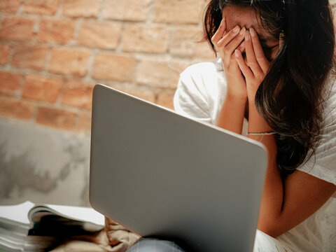 Asian young woman covering her face with her hands, crying, emotional, depressed, stressul, upset, embarrassed and ashamed due to bullying, gossip and harassment on social media. Mental health issue.