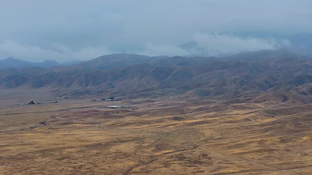 A large, barren desert with a few buildings in the distance. The sky is cloudy and the sun is not visible