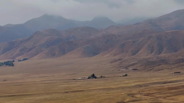 A large, barren desert with a few buildings in the distance. The sky is cloudy and the sun is not visible