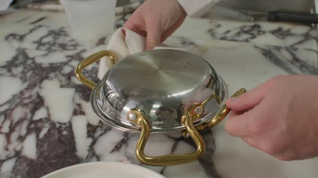 A detailed close-up shot of a chef's hand holding a small silver frying pan with gold handles, skillfully turning a golden-brown frittata