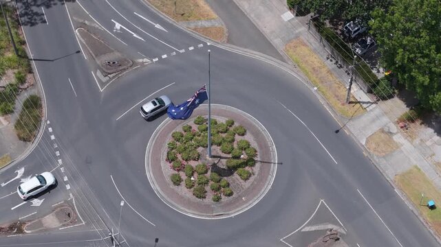 Drone video captures Boronia roundabout in Melbourne, showcasing the Australian flag fluttering atop a sunny landscape. Ideal for urban planning concepts, with steady, wide-angle aerial views.