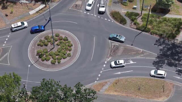Aerial footage of a vibrant roundabout in Boronia, Melbourne, featuring an Australian flag. Cars gracefully navigate the circular road under bright, sunny skies with lush greenery around.