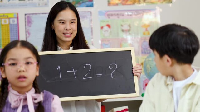 Thai Teacher Holding Chalkboard with Math Equation for Elementary Students in Classroom