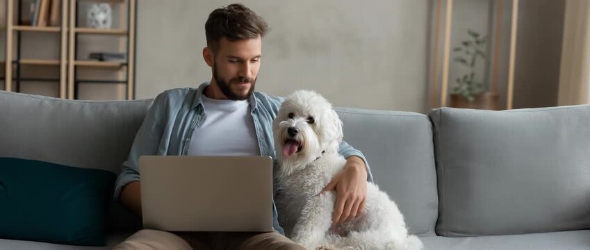 Men using a laptop while sitting on a sofa with his dog at home, remote work