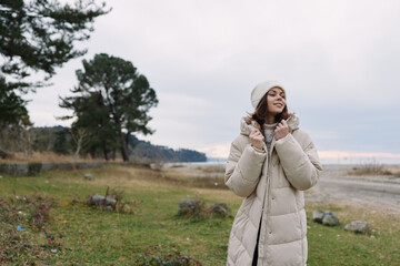Woman in a long puffy winter coat outdoors along a coastline at dusk, enjoying the cool air and distant waves, conveying coziness, calm and fashion in a natural landscape scene.