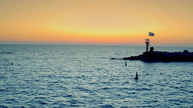 Mesmerizing view of Sunset over the Mediterranean Sea in Israel with a small jetty and the Israeli flag at twilight