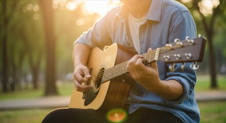 Obraz premium Man plays acoustic guitar outdoors during sunset with lens flare effect