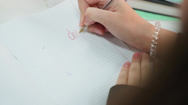 closeup hands practicing math on graph paper notebook, guiding wrist and bracelet visible, careful pen strokes forming numbers, neat classroom desk with pastel stationery, calm focused study