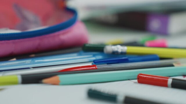 scattered colored pencils near pencil pouch on open notebook, shallow depth closeup with soft pastel tones, tidy and messy supplies mixed, blurred background of classroom materials, tranquil study