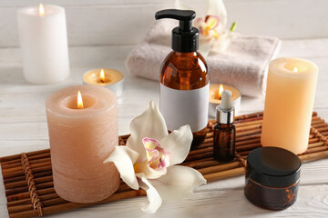 Burning candles with orchid flowers, towel and spa supplies on white wooden background