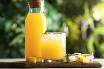 Fototapeta premium Glass and bottle of fresh pineapple juice with mint leaves on white tile table outdoors