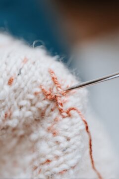 Close up of darning stitch on wool garment with sewing needle in motion, showcasing visible texture and slow fashion repair techniques for sustainable clothing care