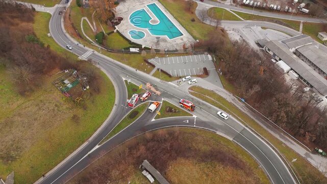 High angle aerial shot of emergency services and fire trucks responding to a vehicle crash and hazardous oil spill at a road junction in Slovenia.