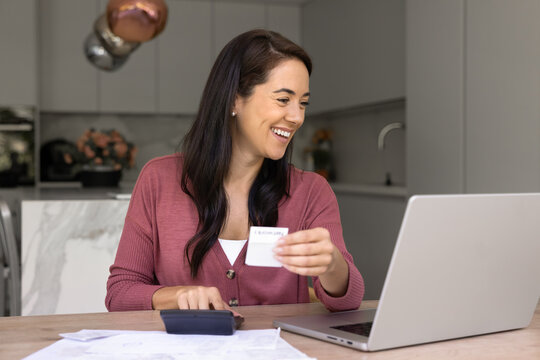 Satisfied middle-aged 40s woman sit at table with laptop, heap of receipts and calculator, holding bill, perform payments through secure online banking. Household finances management, digital epayment
