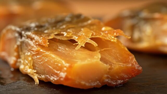 Macro shot of golden smoked fish fillet or delicacy piece with flaky texture, rich flavor, and savory seasoning, presented on a dark slate board, gourmet seafood close-up