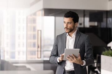 Syrian businessman standing in corporate office with digital tablet, checking and replying to...